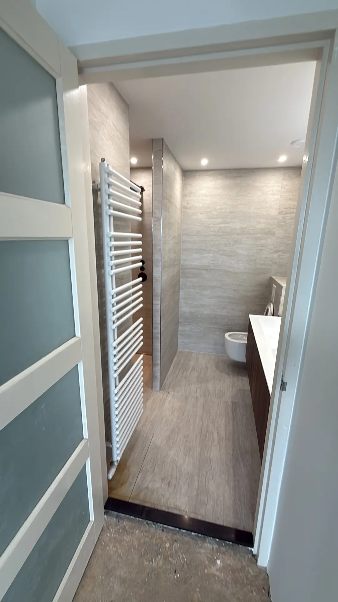 Overzicht gerenoveerde badkamer vanuit de deuropening met designradiator en tegelvloer — project Amsterdam