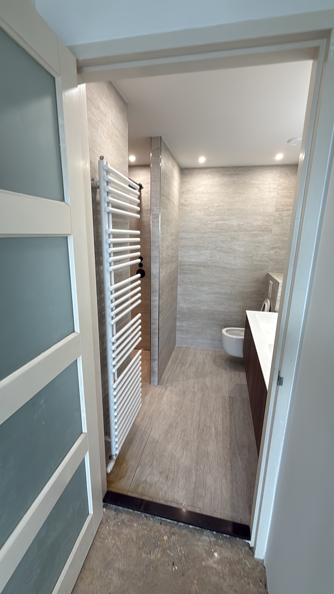 Overzicht gerenoveerde badkamer vanuit de deuropening met designradiator en tegelvloer — project Amsterdam